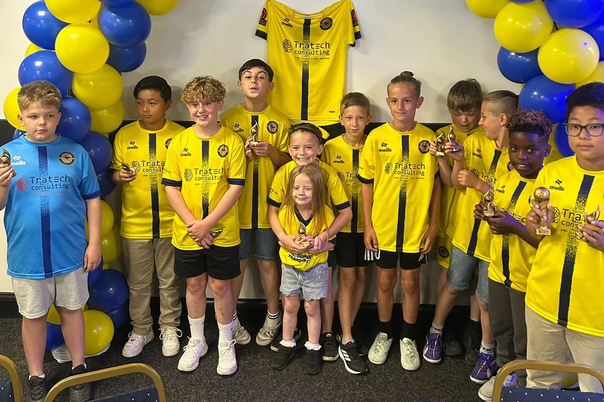 The squad with their trophies under a blue and yellow balloon arch