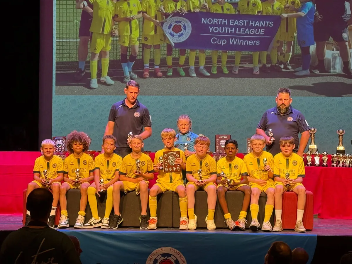 A Junior Academy squad on stage with their trophies as North East Hants Youth League cup winners.