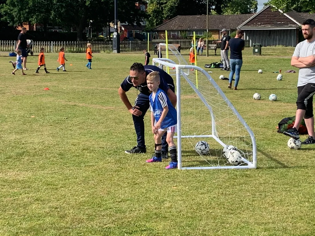 A coach guiding a young player in a shooting drill at training.