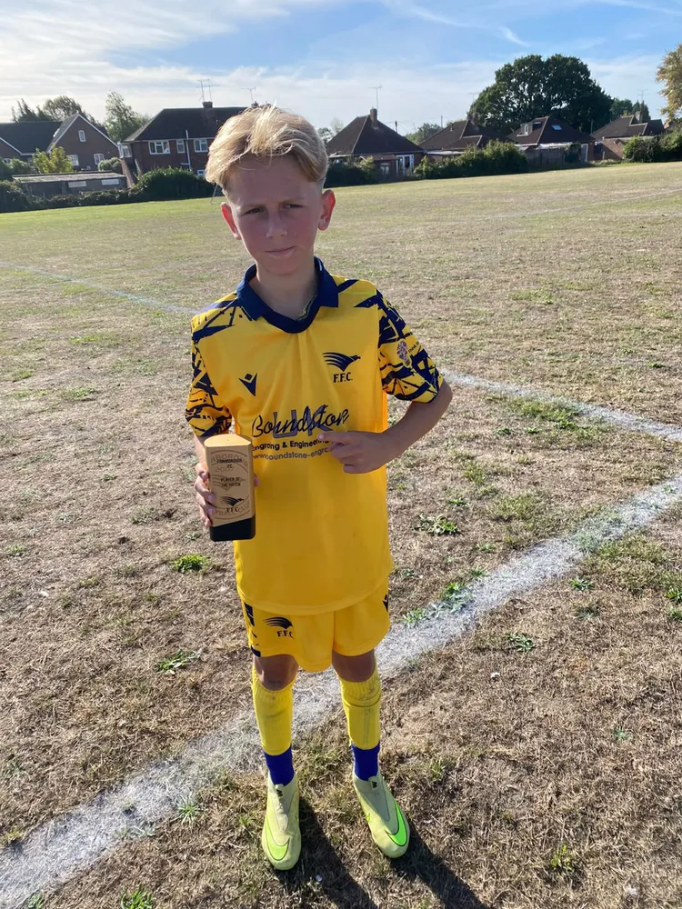 Trophy held out to the camera on a dry, sun-bleached pitch