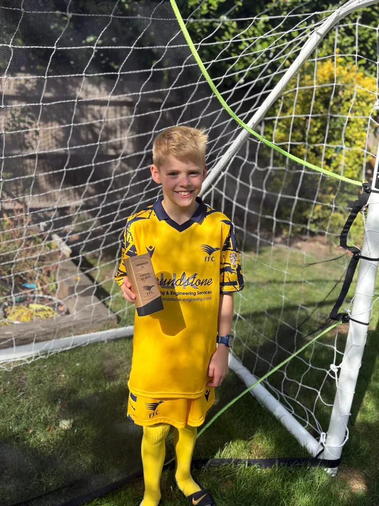 A big grin in front of a garden goal, trophy in hand