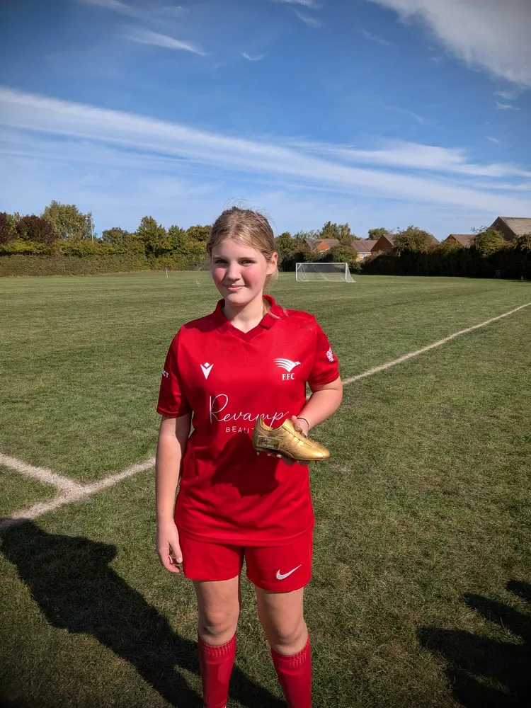In the red kit under a clear blue sky, with a golden boot trophy