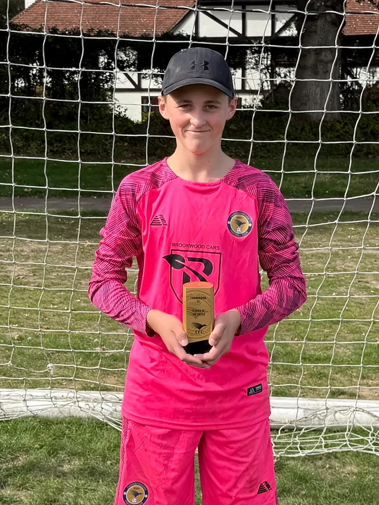 The goalkeeper in a pink kit and cap, trophy in hand in the goalmouth