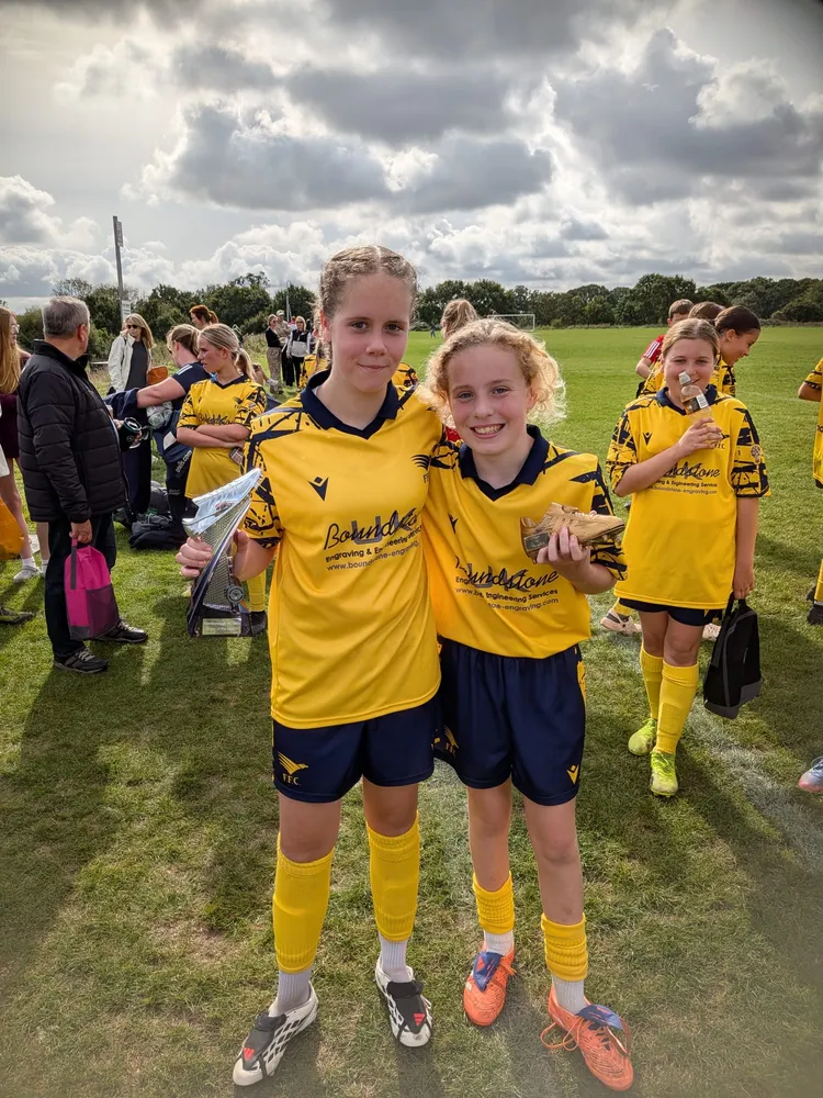 Two team-mates arm in arm under a stormy sky, one with a silver trophy and one with a golden boot