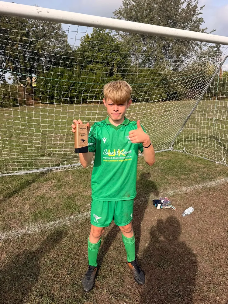 The goalkeeper in green, trophy in one hand and a thumbs up with the other