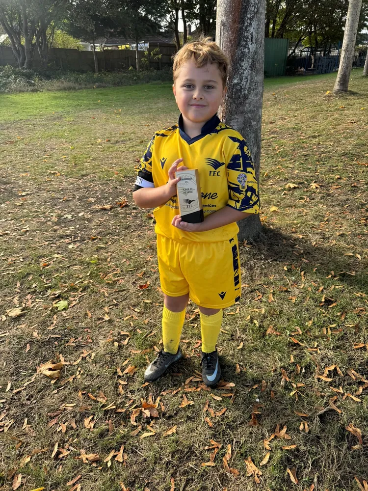 Leaning on a tree among fallen leaves, captain's armband on and trophy held close