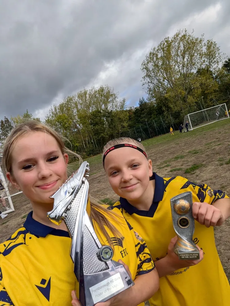 Two girls in a selfie, one with a tall silver boot trophy and one with a Coaches Player of the Match award