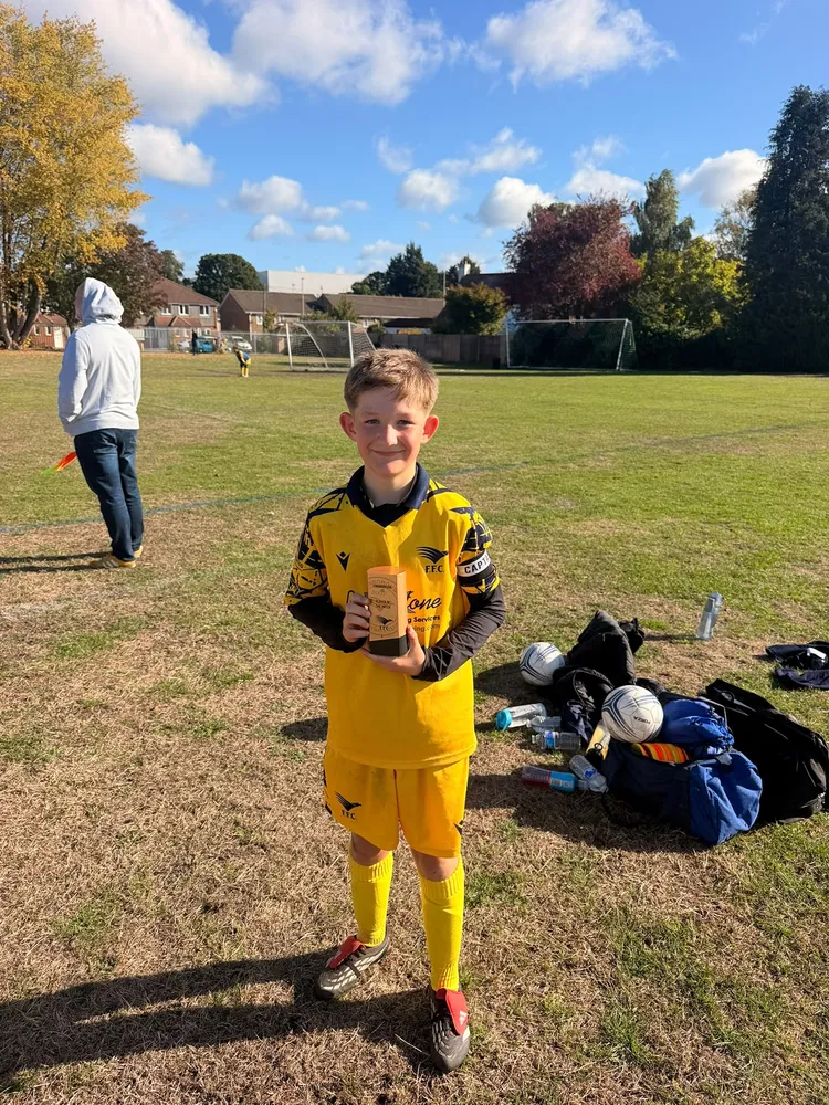 A small black trophy topped with a football, held up with a grin in the autumn sunshine