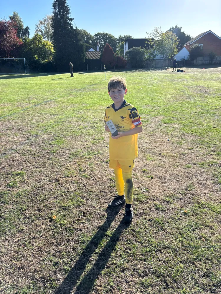 Alone on a wide, sun-baked pitch with a long shadow stretching out behind, the trophy held close