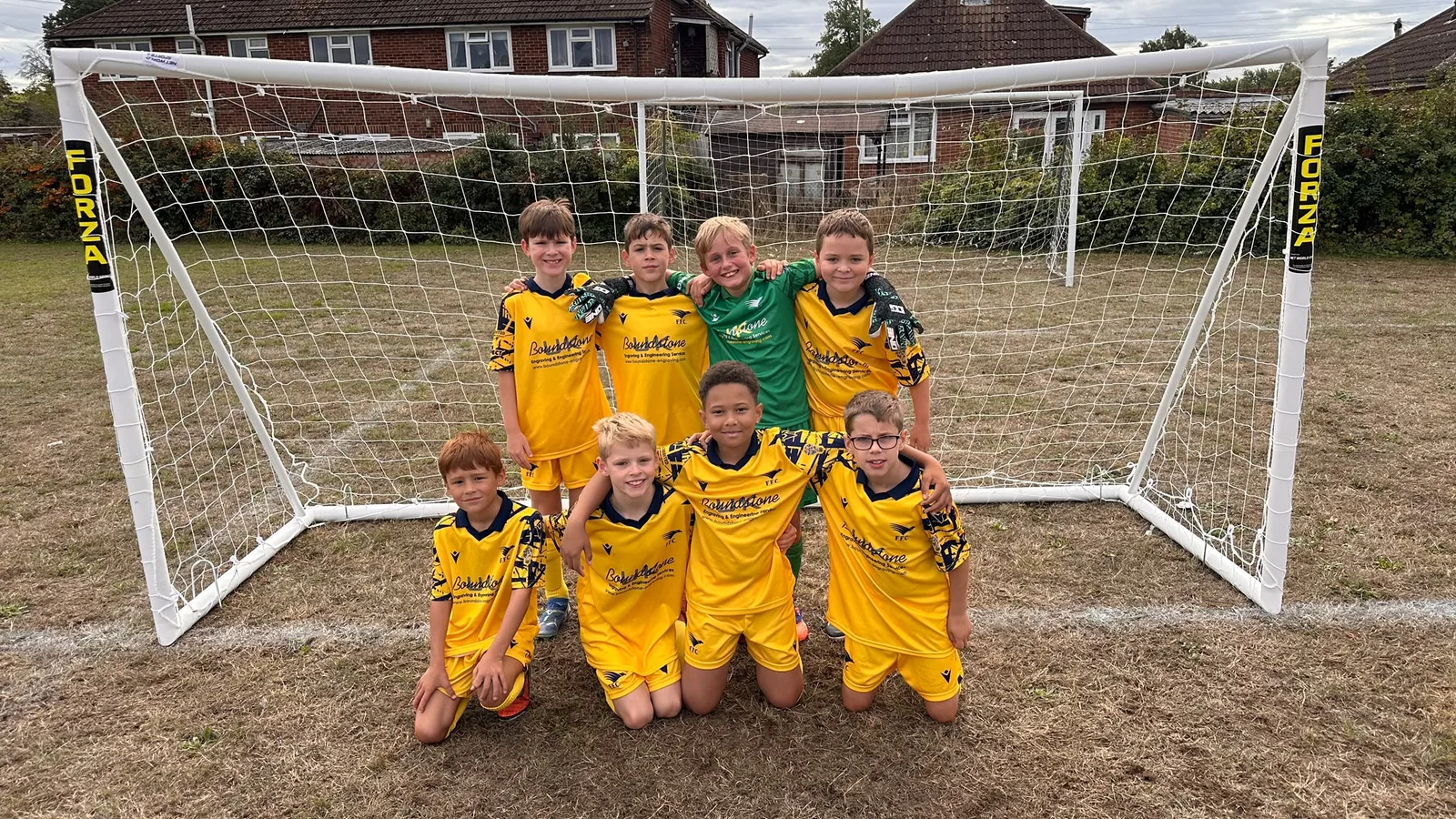 The Under 10 Blues squad in front of the goal, four standing with arms round each other and four kneeling in front, the goalkeeper in green
