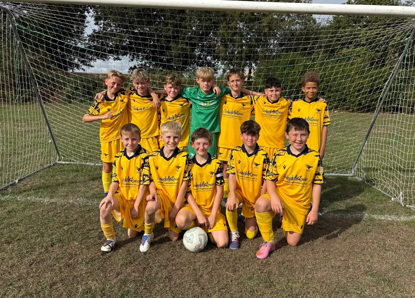 The Under 12 Reds in their yellow Boundstone kit, seven standing arm in arm and five kneeling round the ball, the goalkeeper in green at the back