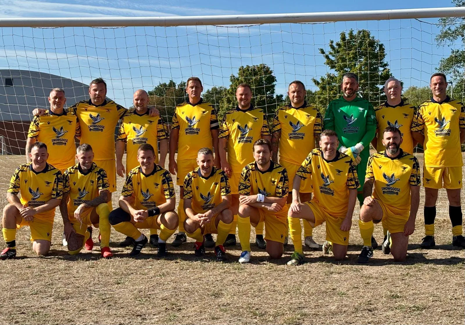 The Vets squad in their yellow Snow Goose kit in front of the goal, two rows, the goalkeeper in green